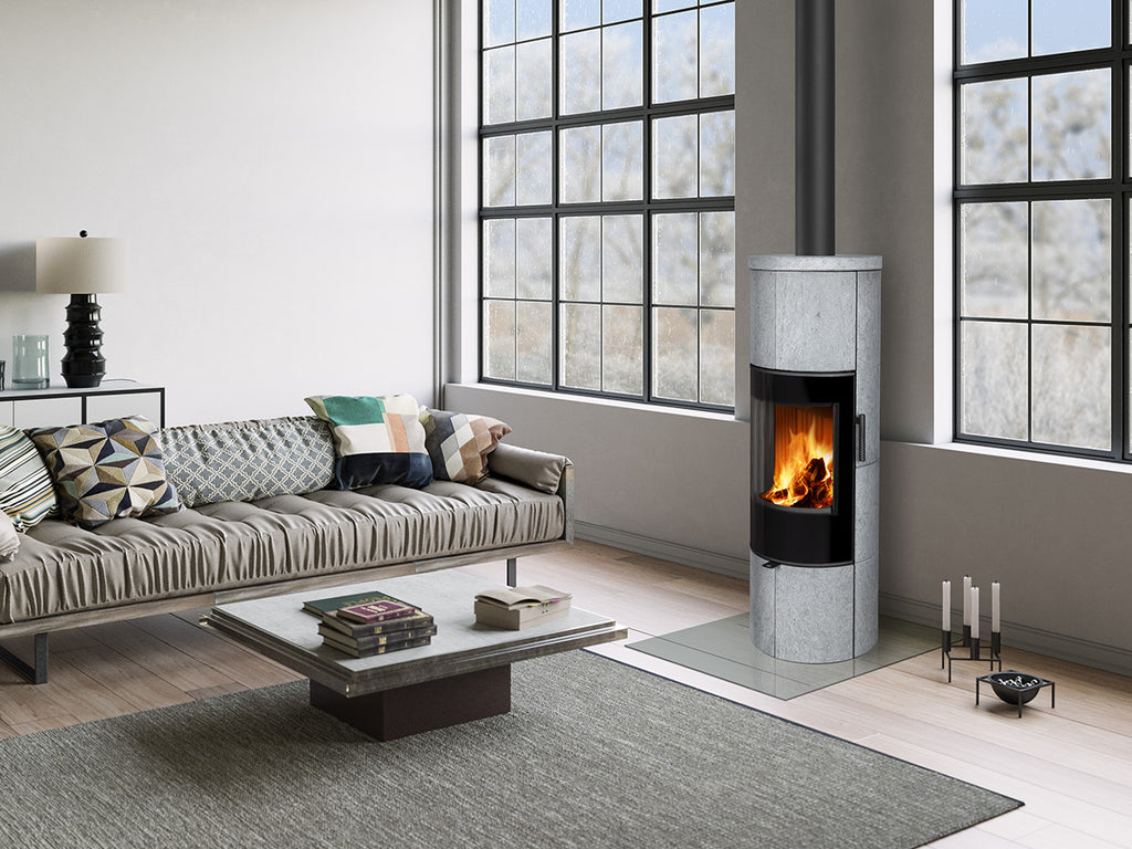 Soba lemne SORIA H, cilindrica, din piatra gri deschis, cu geam mare curbat, usa neagra si foc vizibil, intr-un living modern.