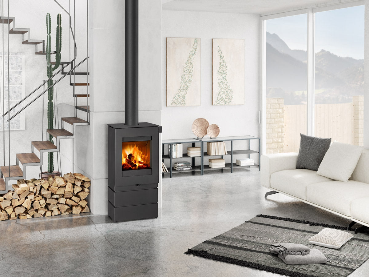 Soba lemne TEON L 03, metal antracit, cu geam si foc vizibil. Integrata intr-un living modern, langa scara si lemne, cu vedere spre munti.